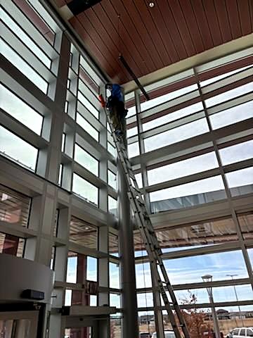 JB's crew cleaning a high glass wall from a ladder